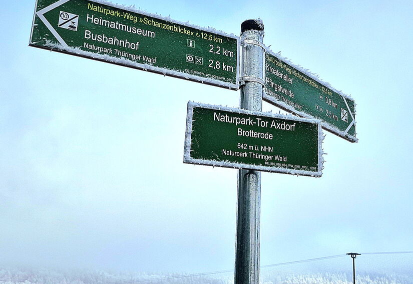 Wanderwegweiser im Winter, im Hintergrund der Thüringer Wald mit Raureif