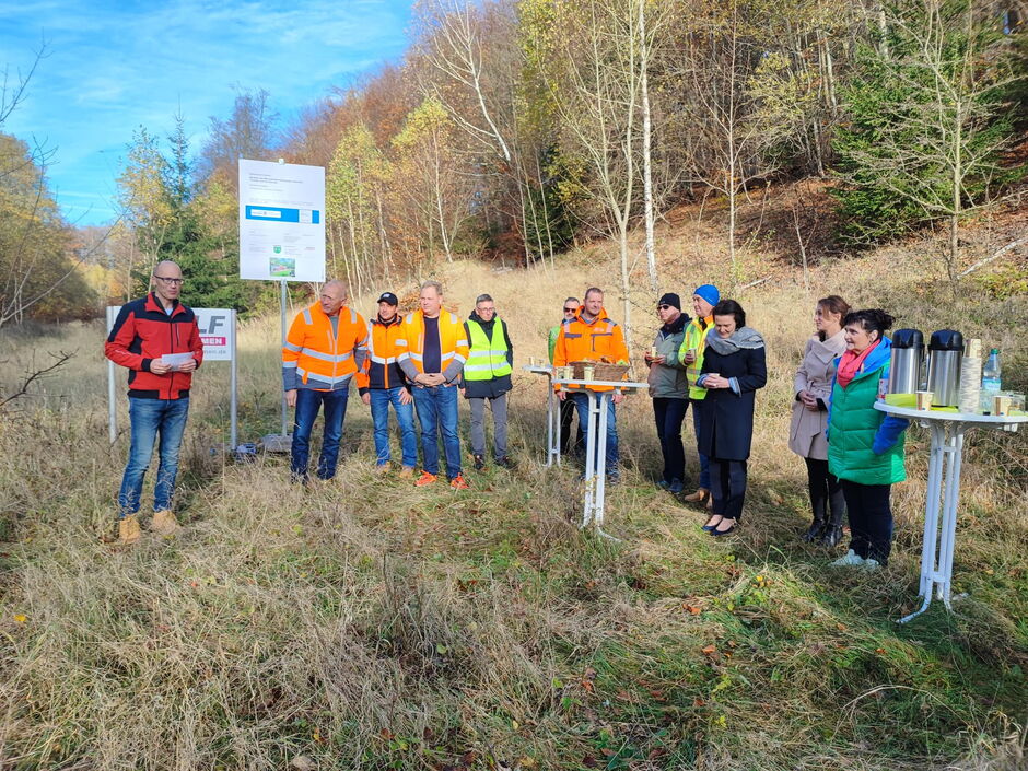 Landrätin Peggy Greiser, der beauftragten Baufirma Wolf und eine Reihe anderer Interessierter beim Baggerbiss durch Bürgermeister Kay Goßmann.
